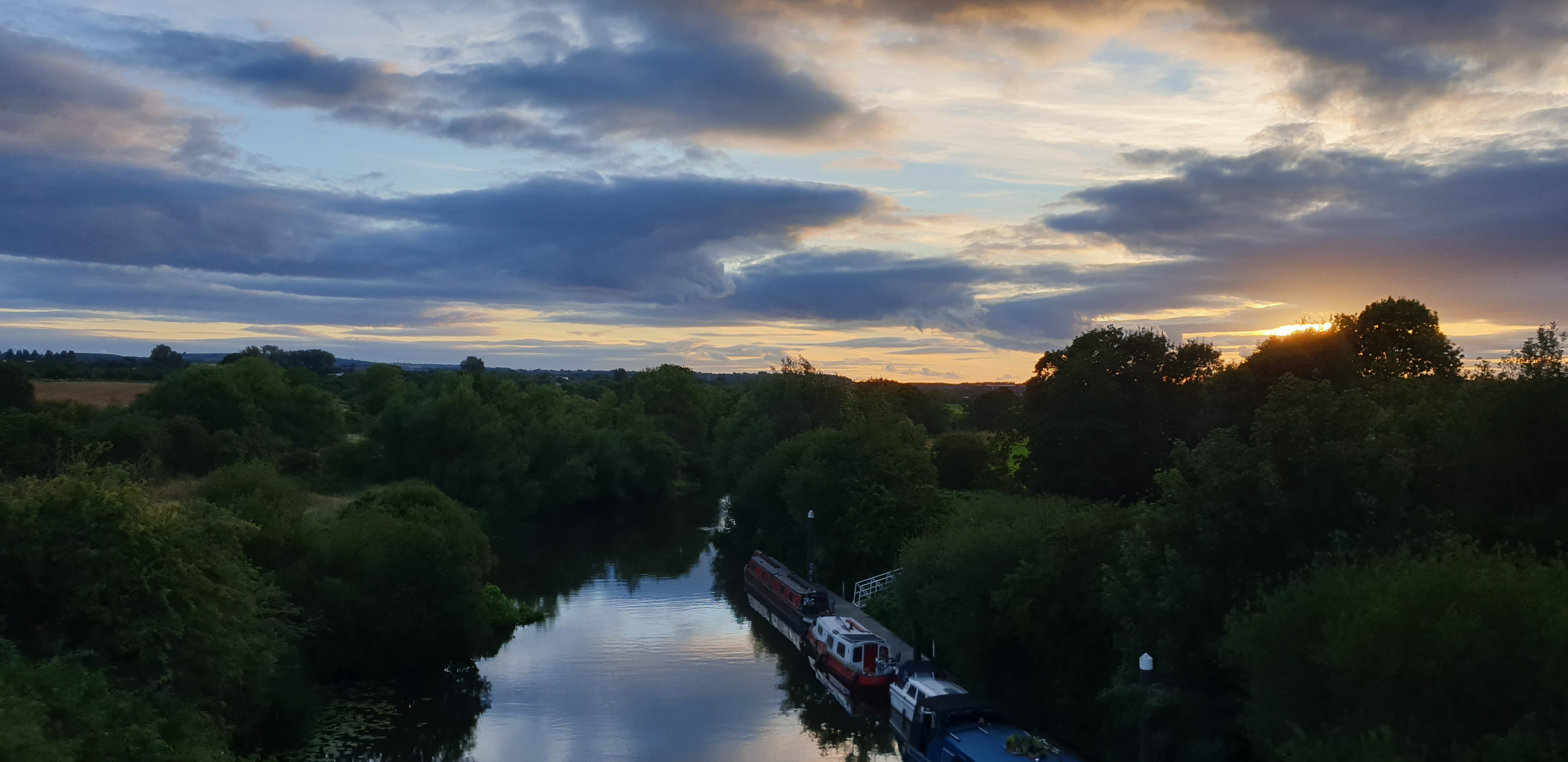 a photo of the river avon at dusk with the blue/orangesky and clouds reflecting on the calm surface